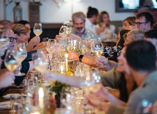 Traverse City Food & Wine Festival: Looking Back on Its Inaugural 2025 and Forward to 2026 A group of people sitting at a table and raising their wine glasses for a toast.